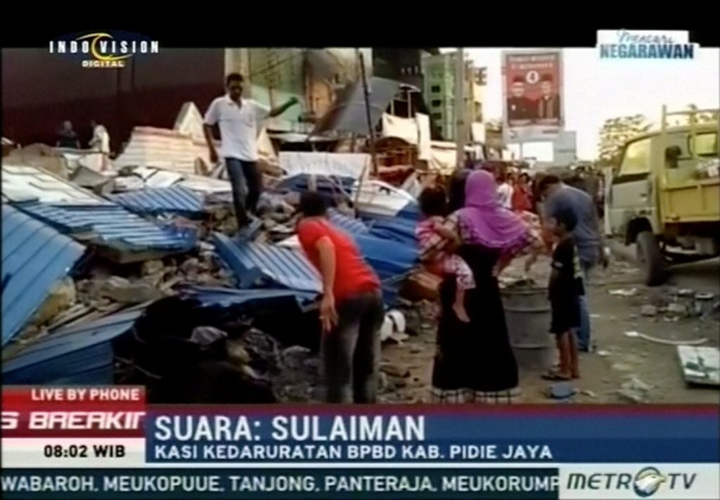 People stand next to rubble of collapsed buildings following an earthquake in Pidie Jaya, Aceh, Indonesia in this still frame taken from video